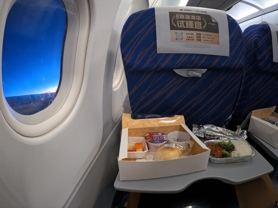 Eine Flugzeugkabine mit Essen auf einem Tablett und einem Fenster bei Sonnenuntergang.