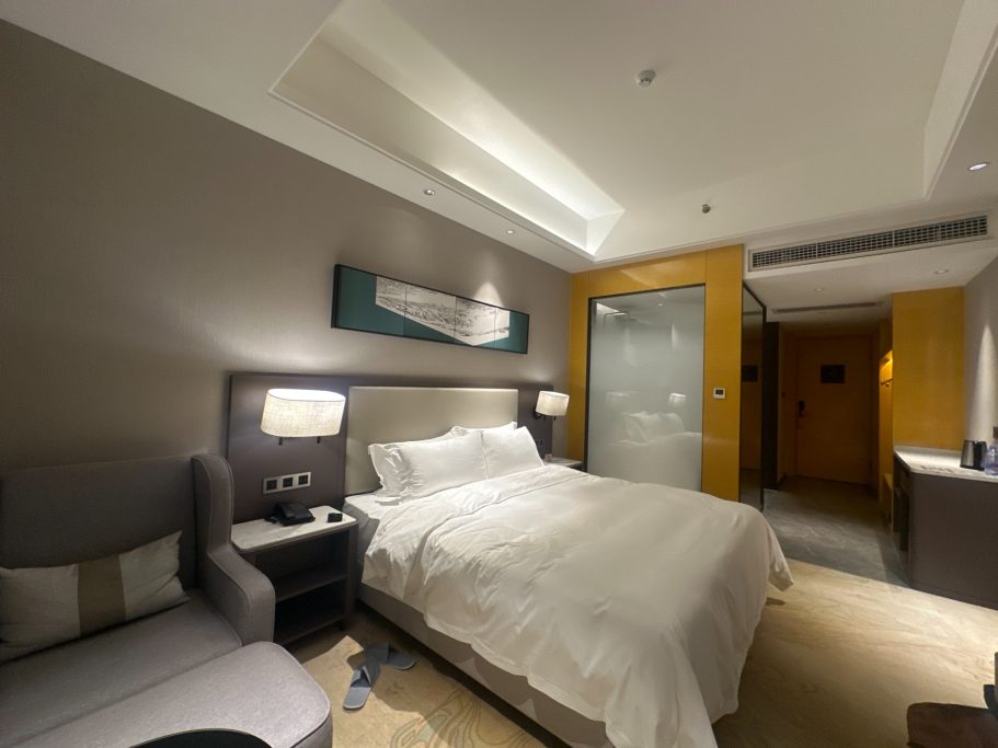 Helles Hotelzimmer mit Doppelbett, Sessel und moderner Dusche.