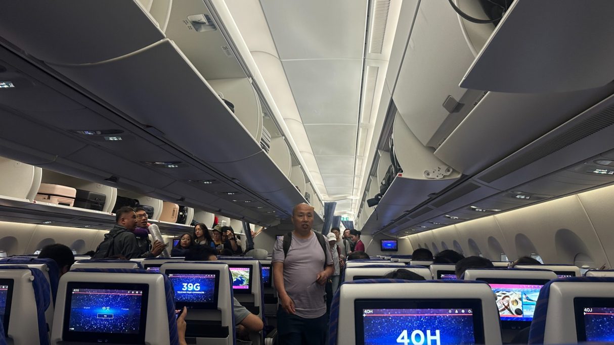 Blick ins Innere eines Flugzeugs mit Passagieren und Monitoren an den Sitzen.