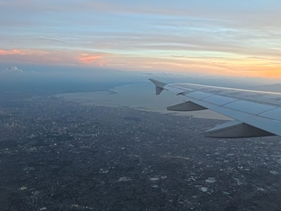 Flugzeugflügel über einer Küstenlandschaft bei Sonnenuntergang.