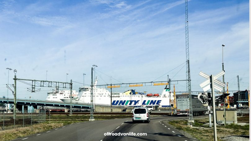 Fährterminal mit einem großen Schiff und Verkehrshinweisen im Vordergrund.